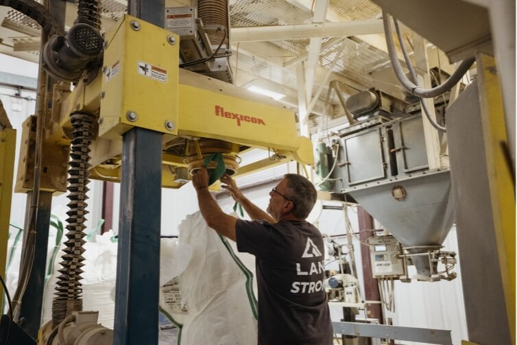 A man removing a bag from a yellow piece of machinery in a processing plant.