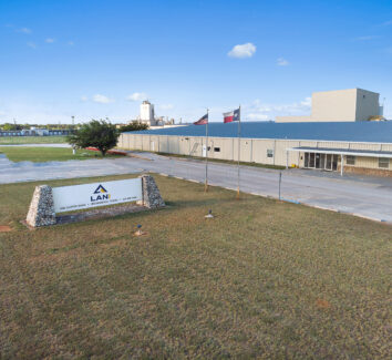 A processing plant with a LANI sign, an American flag and a Texas flag on the front lawn.