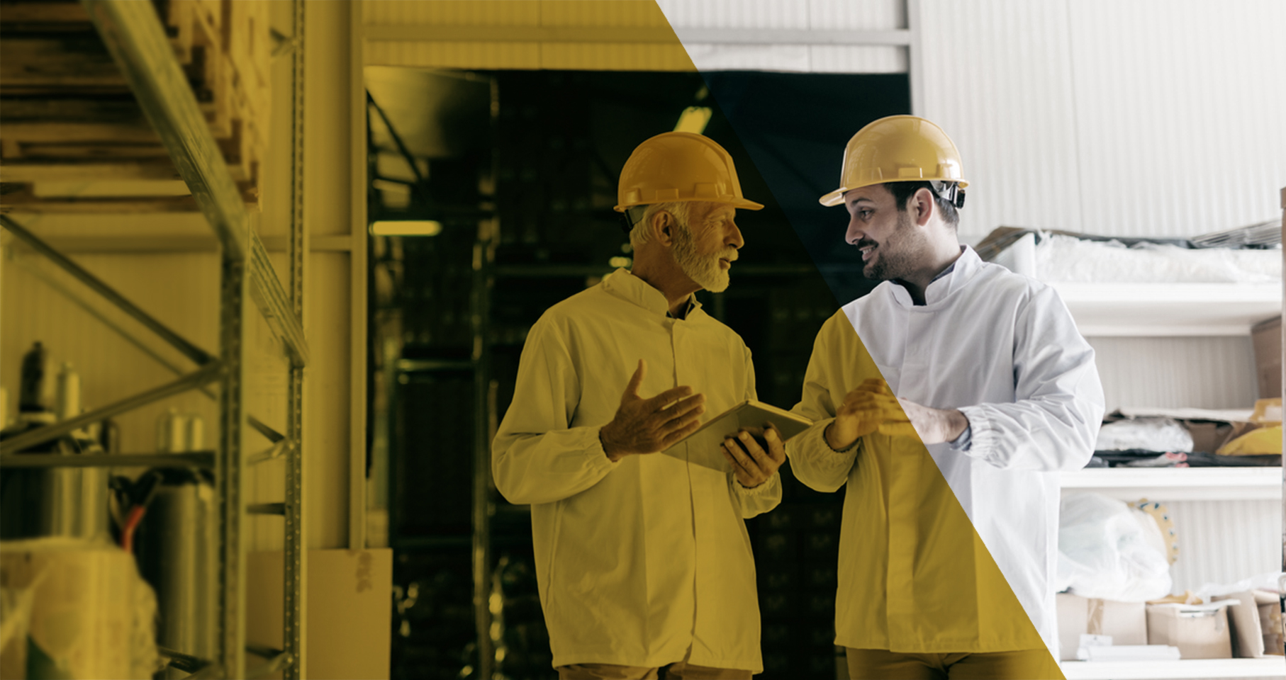Two men weating hard hats and white coats talking in a processing plant.